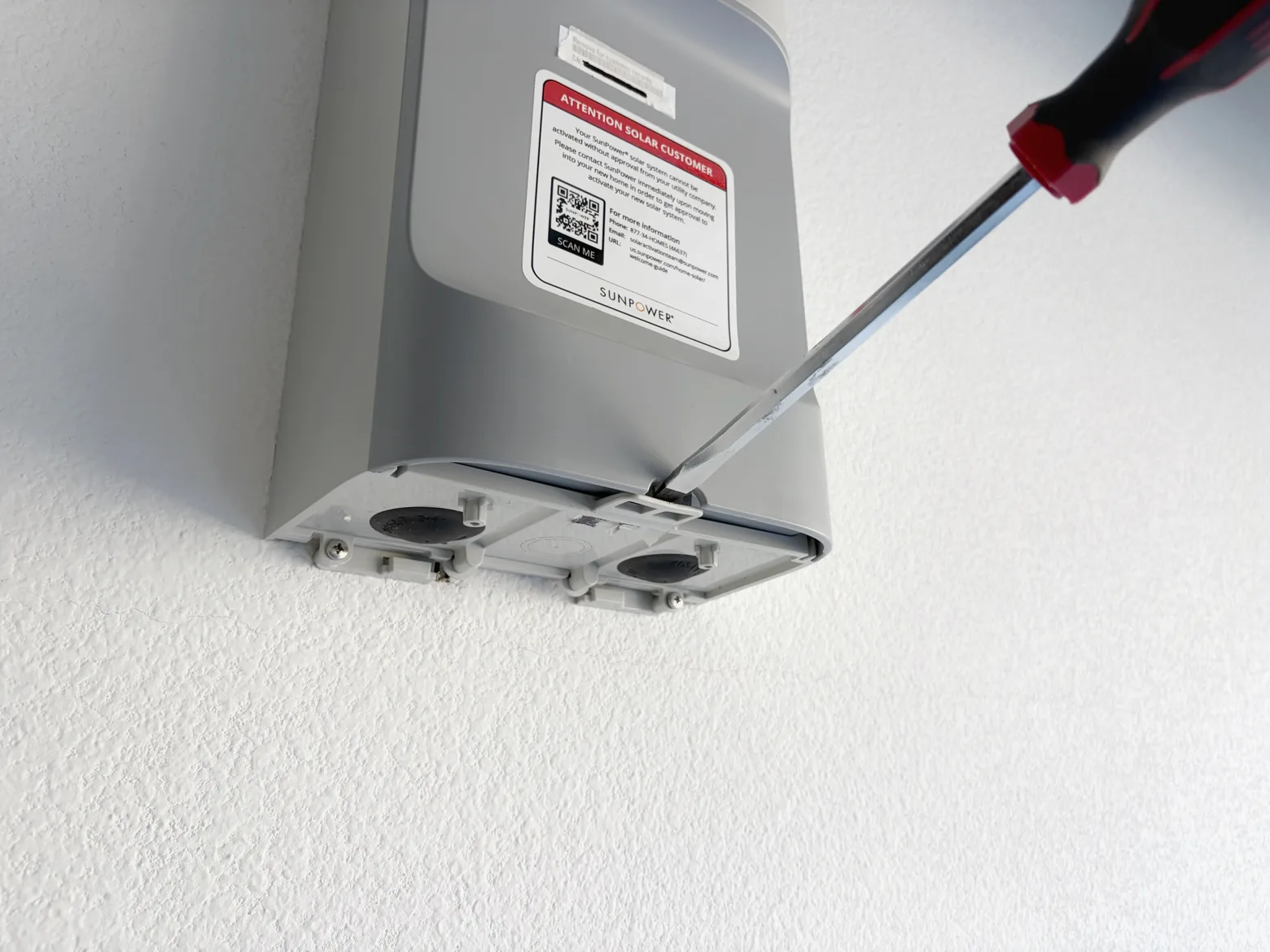 A flathead screwdriver shimmed into the release slot along the bottom edge of the PVS faceplate.